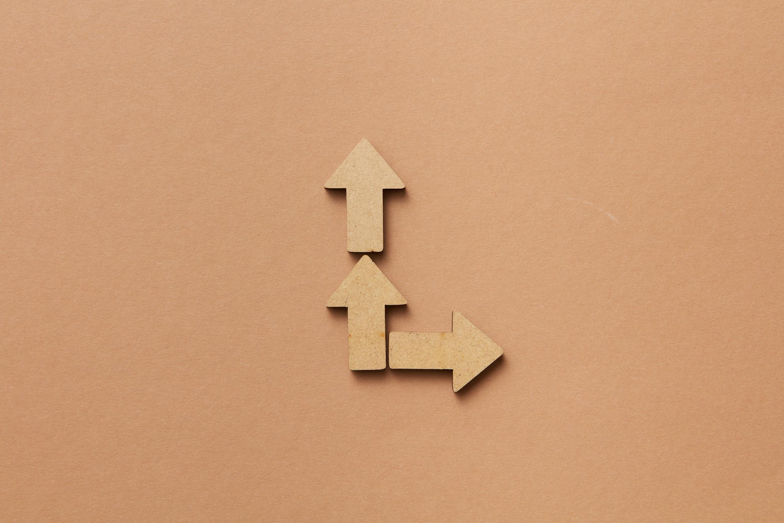 Three cardboard arrows arranged on a brown background, symbolizing direction and choice.