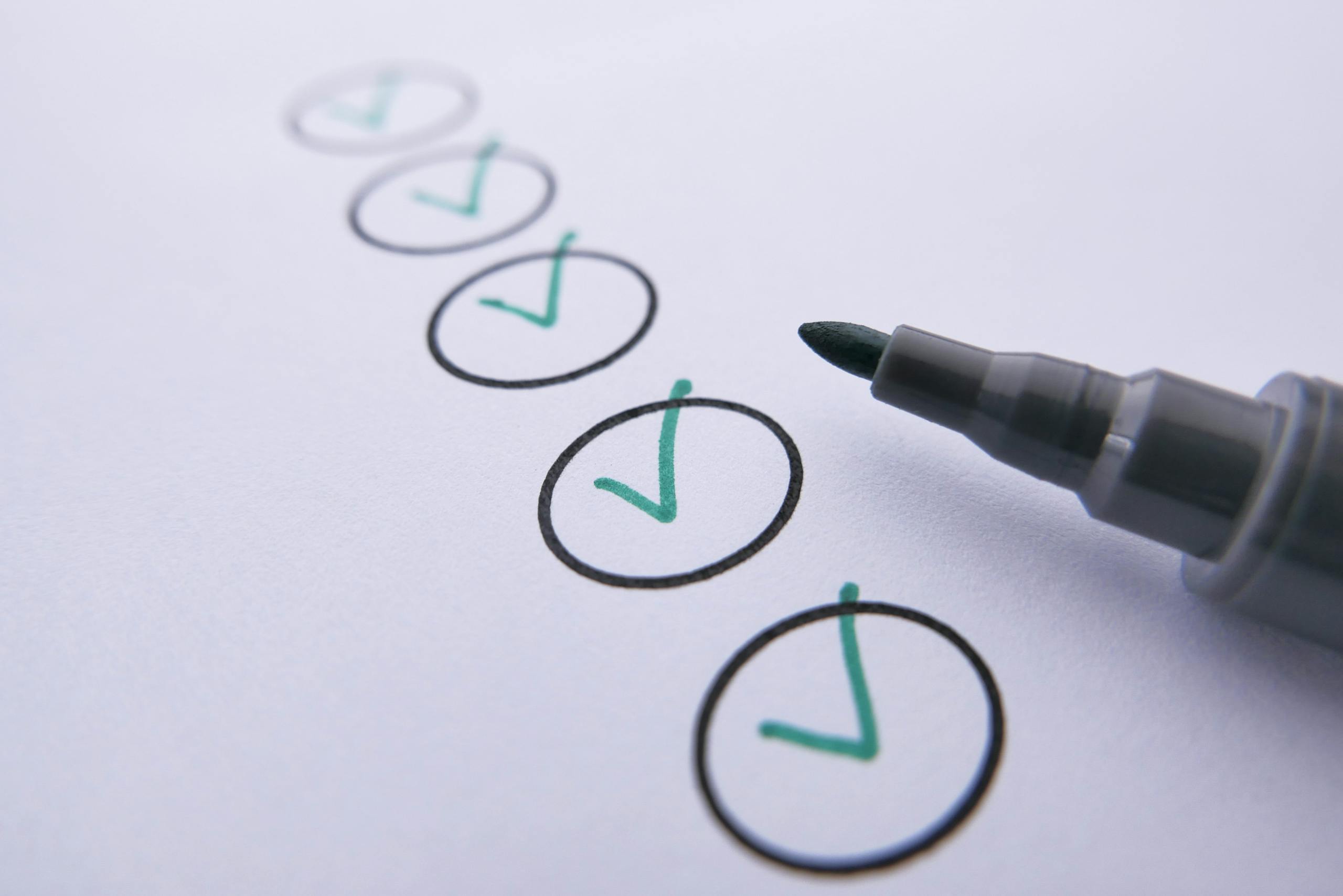 Close-up of a checklist with green checkmarks on white paper using a marker.