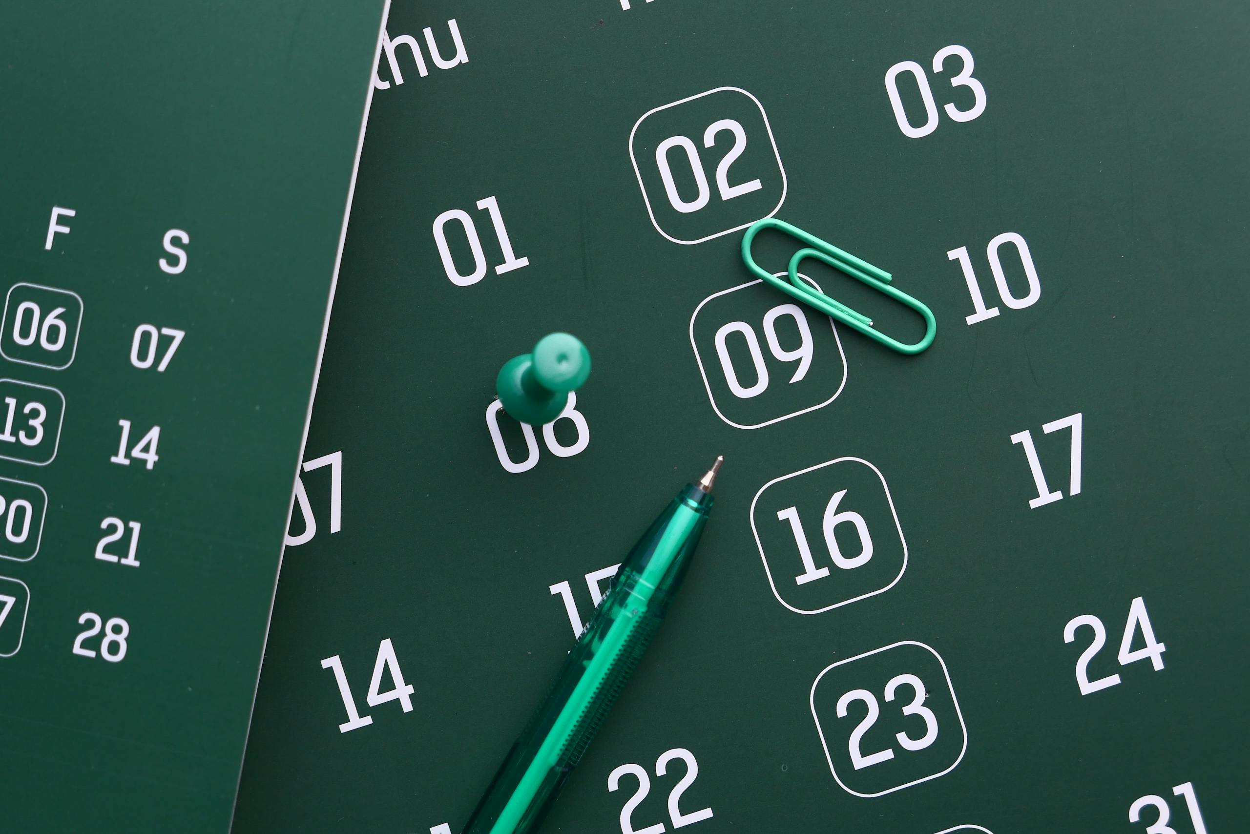 Close-up of a green calendar with pen, push pin, and paper clip for planning and organization.
