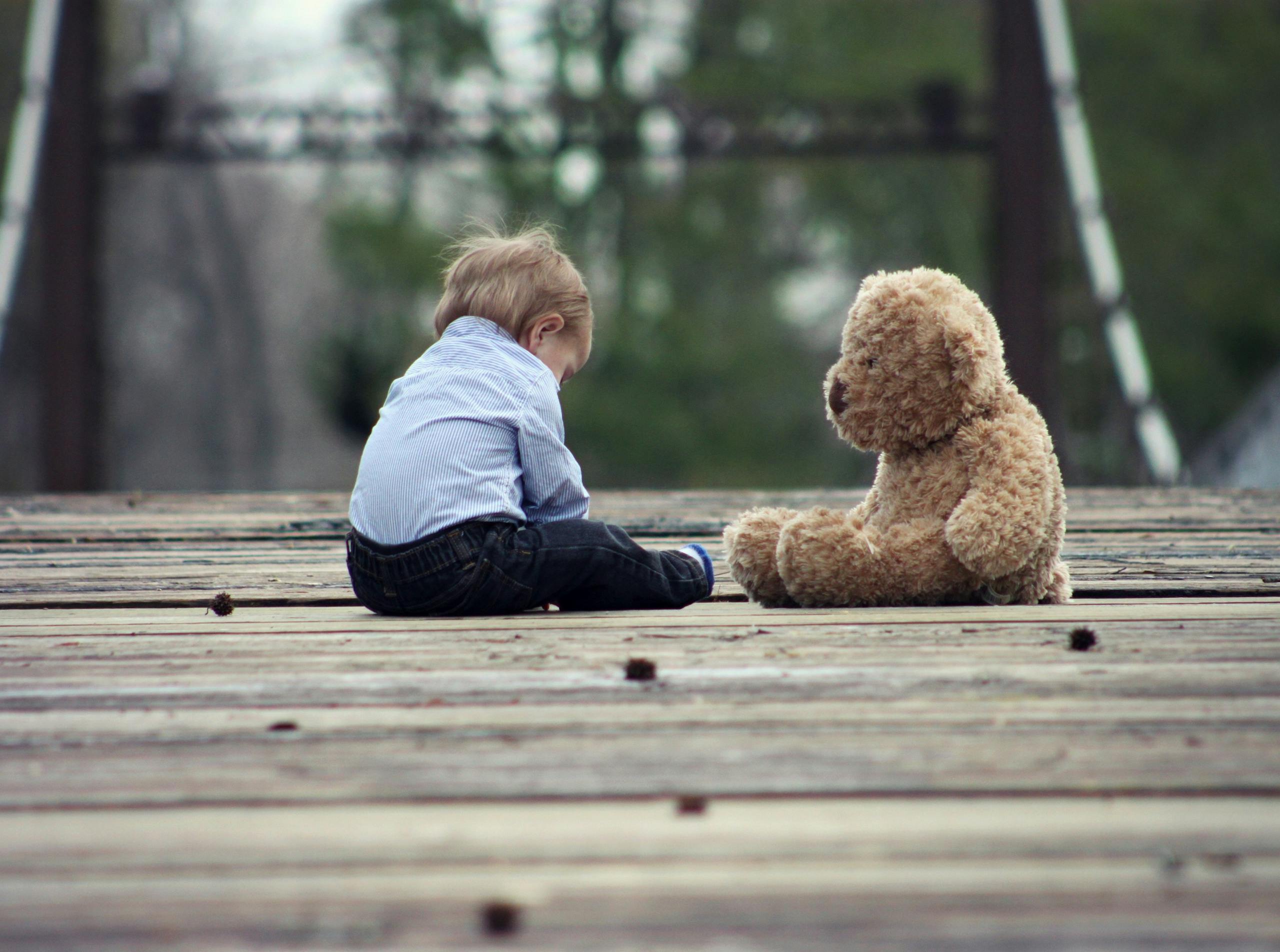 Adorable toddler sitting with a teddy bear on a wooden bridge, enjoying a peaceful moment outdoors.