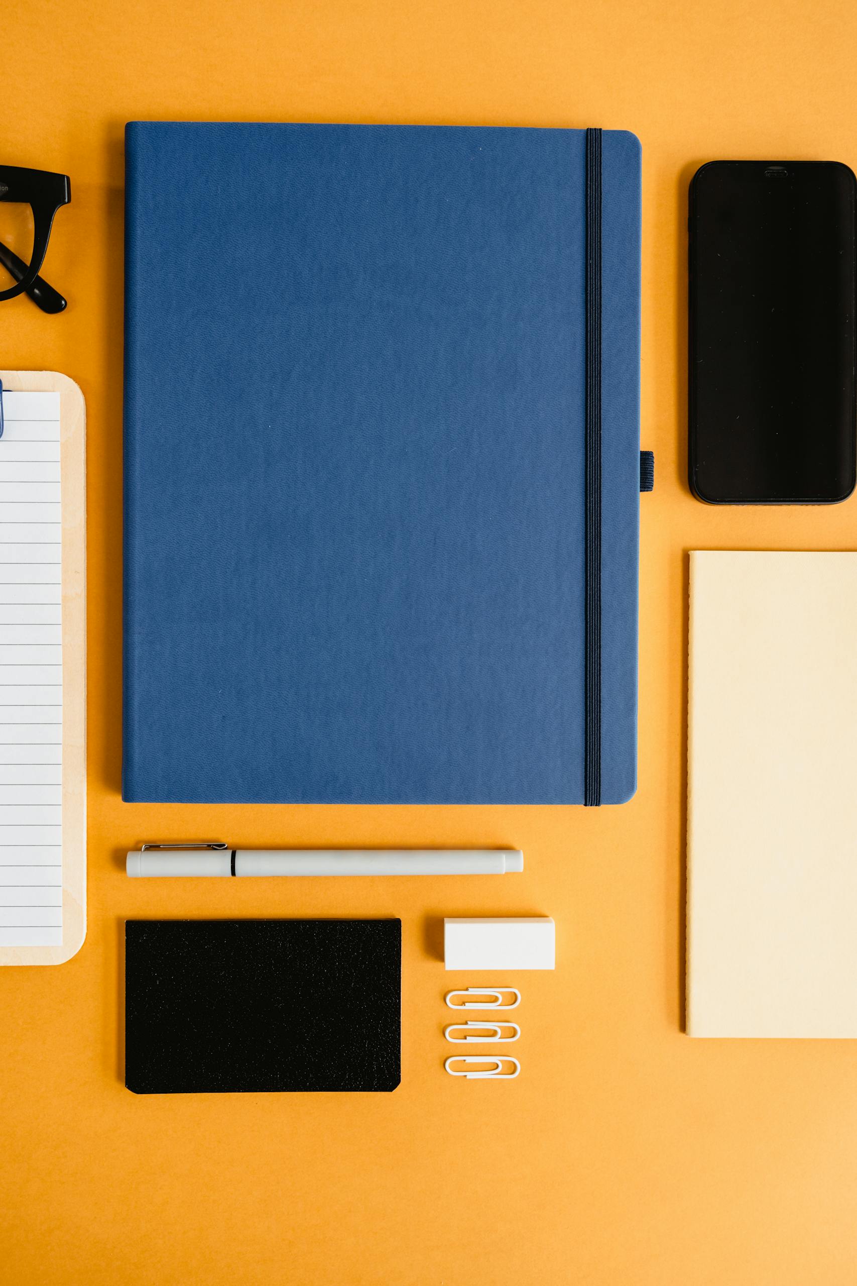 Stylish flat lay of office supplies including notebooks and stationery on a vibrant orange surface.