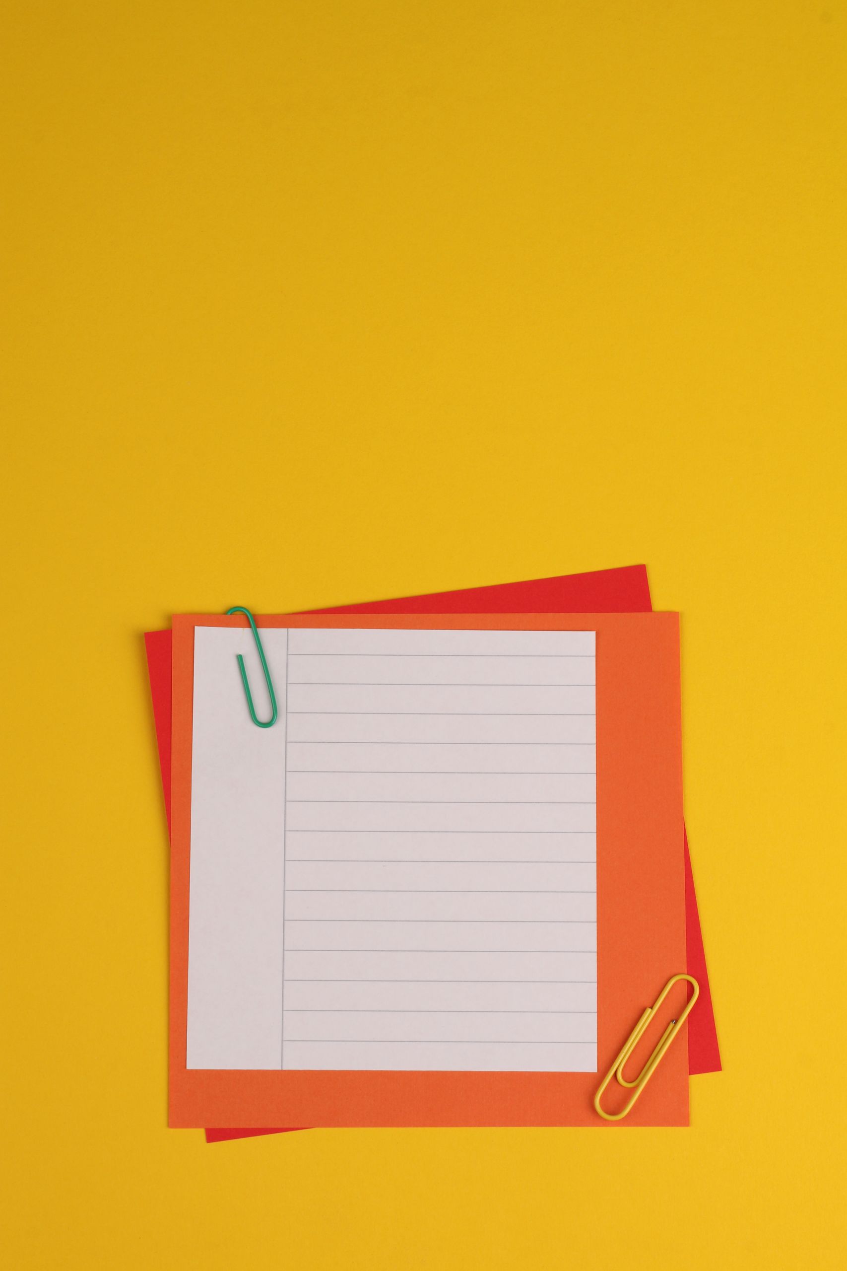 Vibrant arrangement of lined paper and colored paperclips on a yellow backdrop, perfect for creative projects.